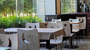 A restaurant with tables and chairs, large windows, and greenery outside.