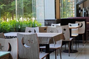 Un restaurant avec des tables et des chaises, de grandes fenêtres et de la verdure à l’extérieur.