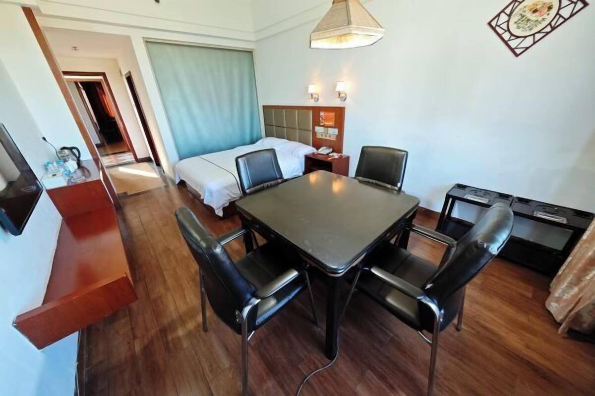A hotel room with a bed, a dining table with chairs, a TV, and a desk with a computer.