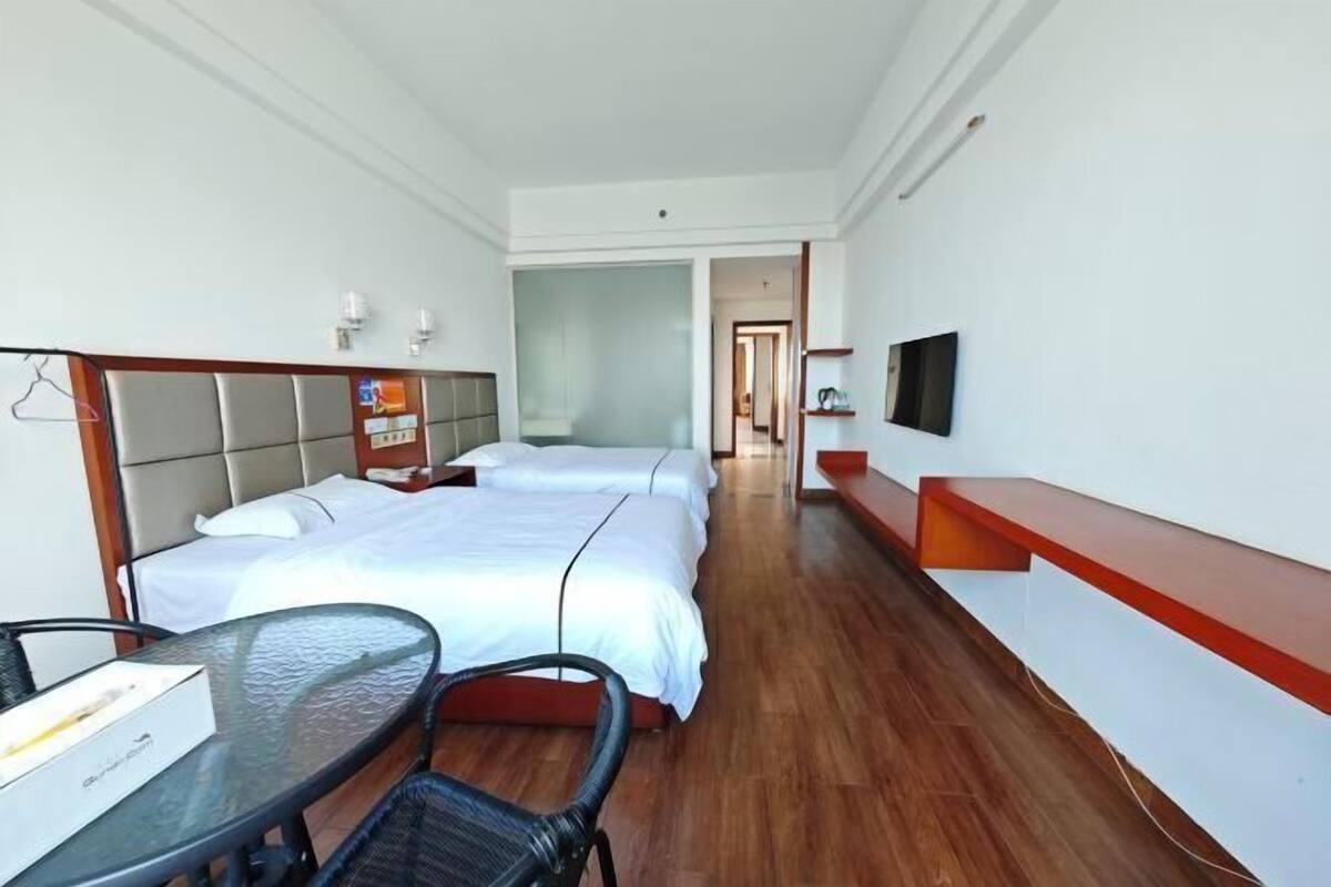 A hotel room with two beds, a TV, a glass table, and a chair.