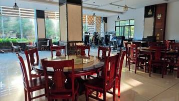 A spacious dining area with round tables and chairs, large windows with a view of greenery, and a modern interior design.