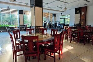 Un comedor amplio con mesas y sillas redondas, ventanas grandes con vistas a zonas verdes y un diseño interior moderno.
