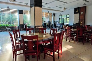 Uma ampla área de refeições com mesas e cadeiras redondas, grandes janelas com vista para o verde e um design de interiores moderno.