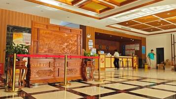 A hotel lobby with a reception desk, a large wooden panel with artwork, and a check-in counter.