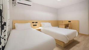 Quarto de hotel com duas camas de solteiro, cabeceira de madeira, uma pequena escrivaninha e ar condicionado.
