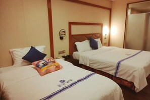 Duas camas de solteiro com roupa de cama branca e detalhes azuis, uma luminária fixada na parede e um objeto decorativo pequeno na cama à esquerda.