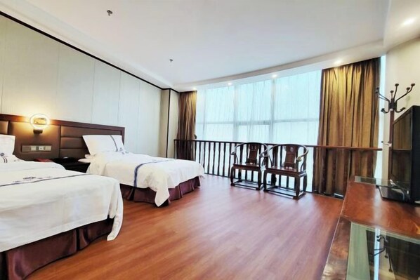 Quarto de hotel com duas camas, uma varanda com cadeira e televisão.