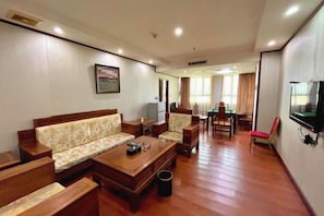 A hotel room with a sofa, chairs, a TV, a dining table, and a trash bin. - Jinjiang Hotel (Taishan)
