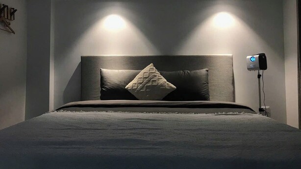 A modern bedroom with a large bed, two bedside lamps, and a ceiling-mounted projector. - The Eudora Homestay (Hai Phong)