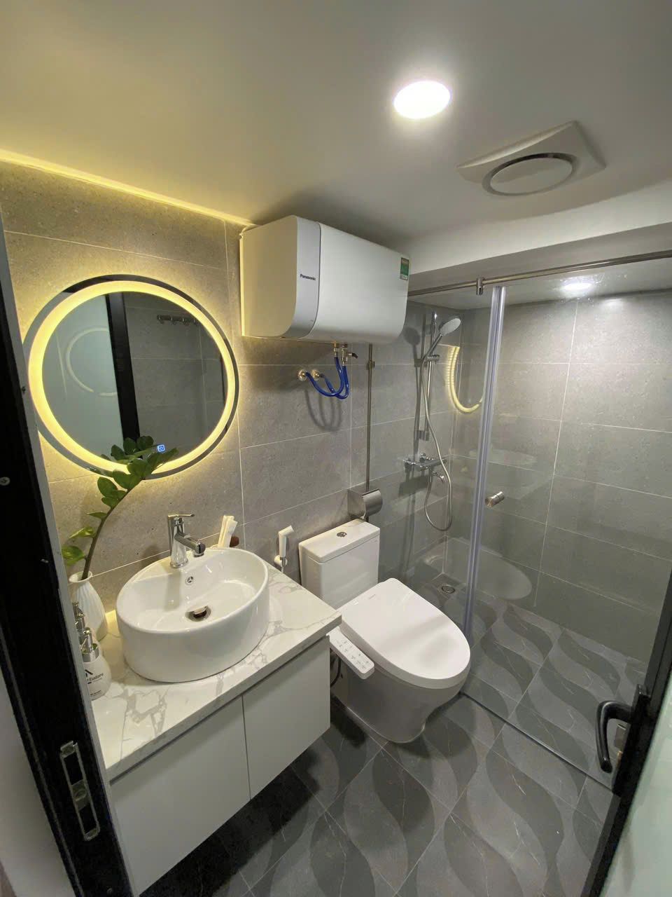 Un baño moderno con un espejo redondo, un lavabo, un inodoro y una ducha con mampara de cristal.