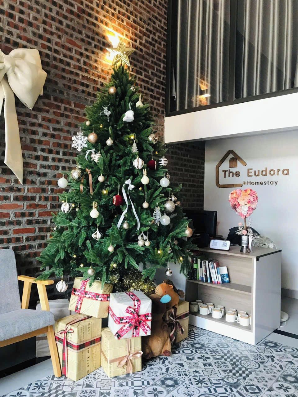 A Christmas tree with ornaments and presents, a reception desk, and a brick wall.