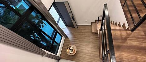 A modern interior with a staircase, a round table with a small plant, and a large window.