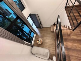 Un interior moderno con una escalera, una mesa redonda con una planta pequeña y un ventanal grande.