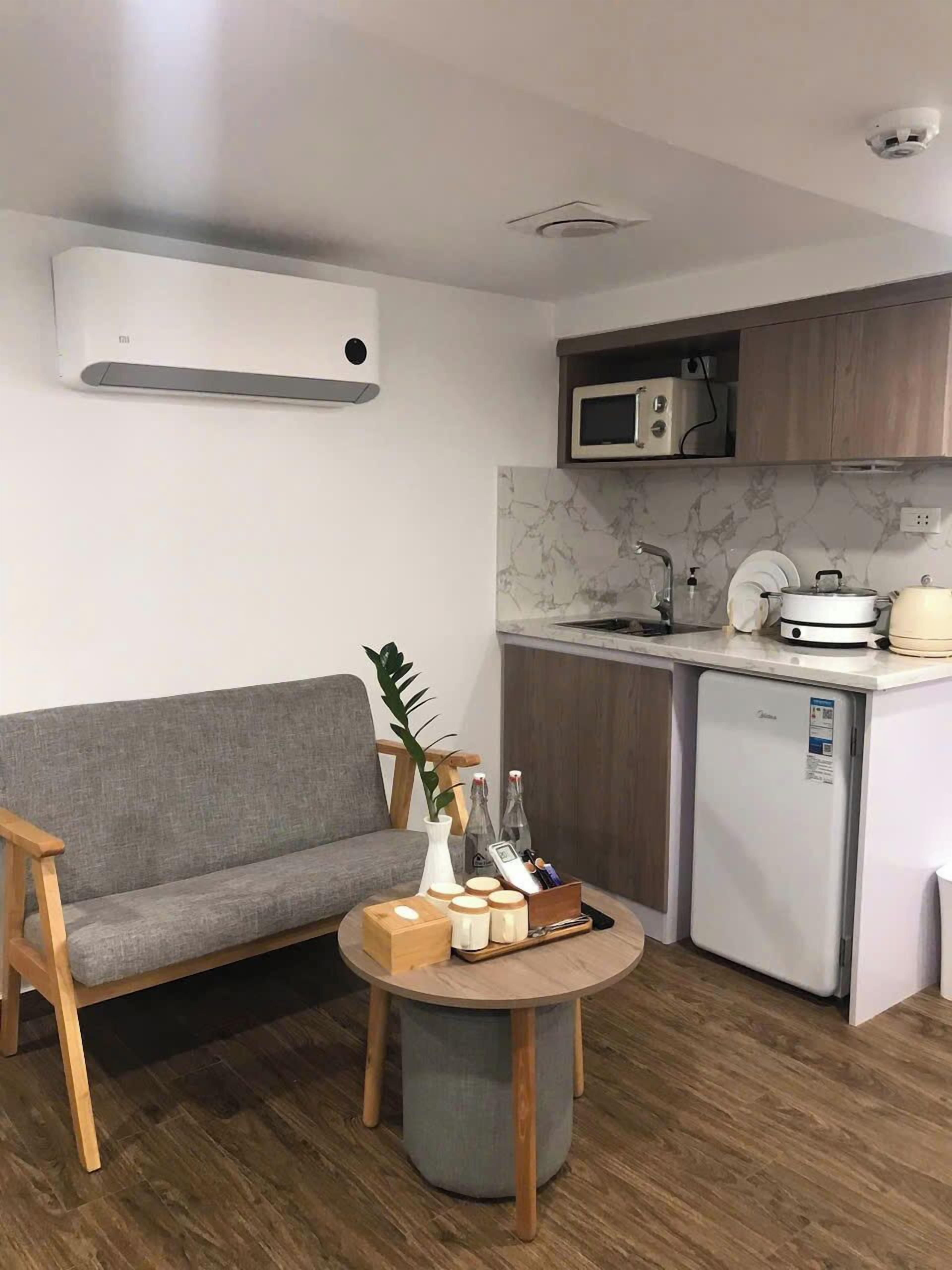Una cocina compacta con un sofá gris, una mesa redonda de madera y un refrigerador pequeño.