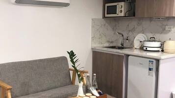 Una cocina compacta con un sofá gris, una mesa redonda de madera y un refrigerador pequeño.