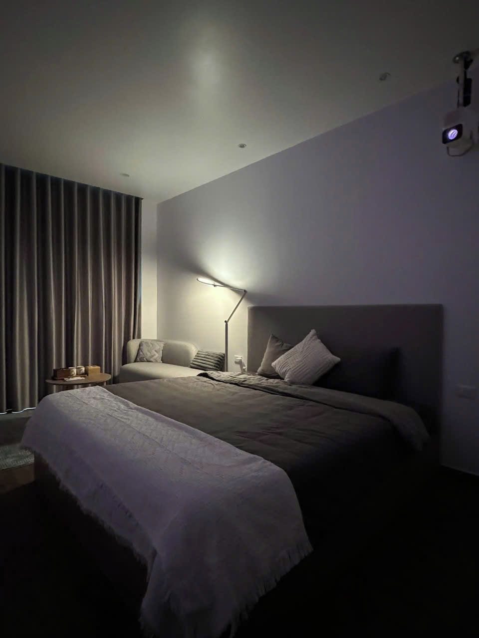 Un dormitorio moderno con una cama grande, una mesita de noche, una lámpara y una ventana con cortinas.
