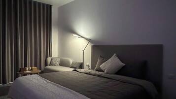 Un dormitorio moderno con una cama grande, una mesita de noche, una lámpara y una ventana con cortinas.