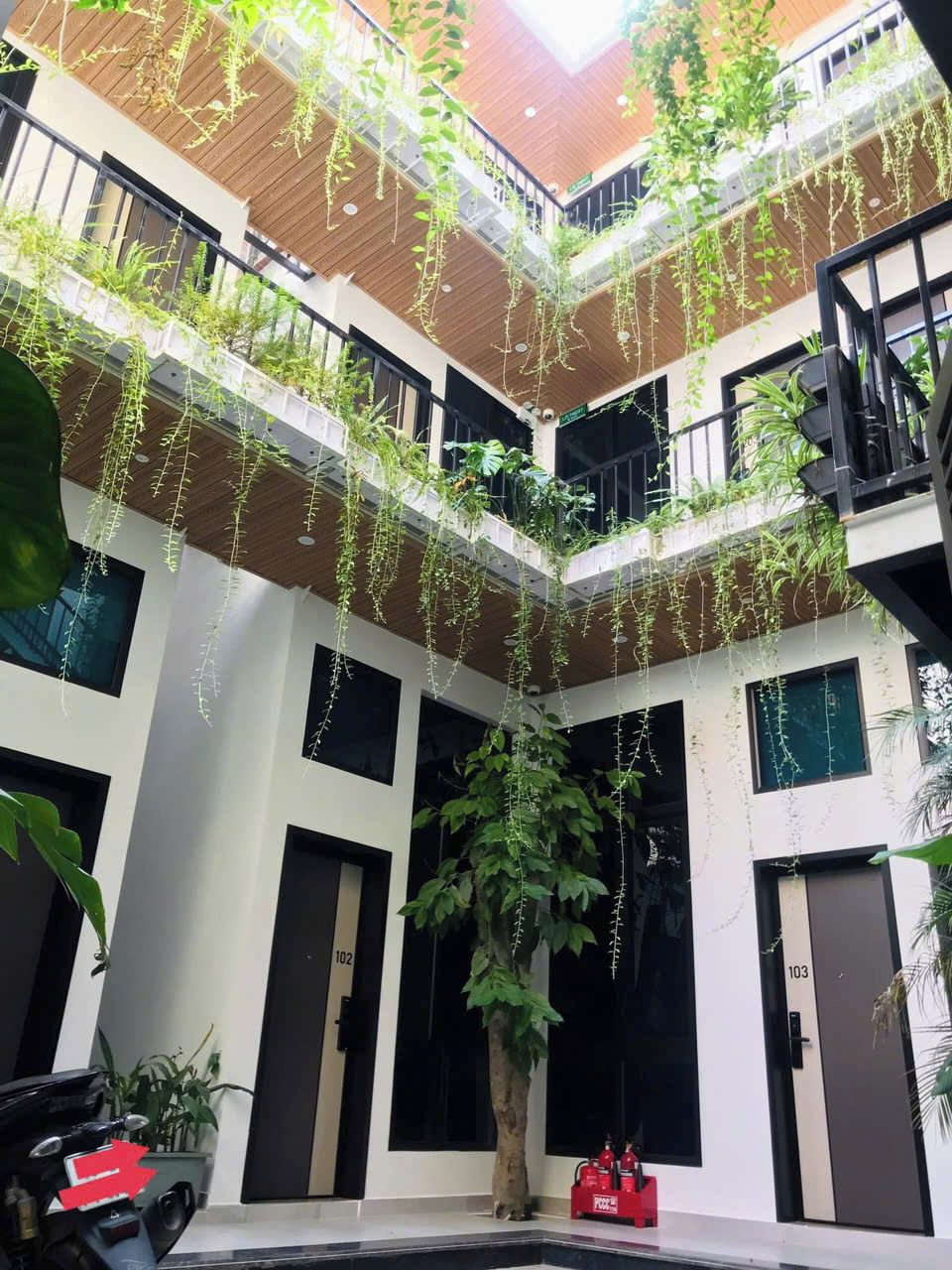 A multi-level atrium with hanging plants and a central tree, featuring balconies and a fire extinguisher.