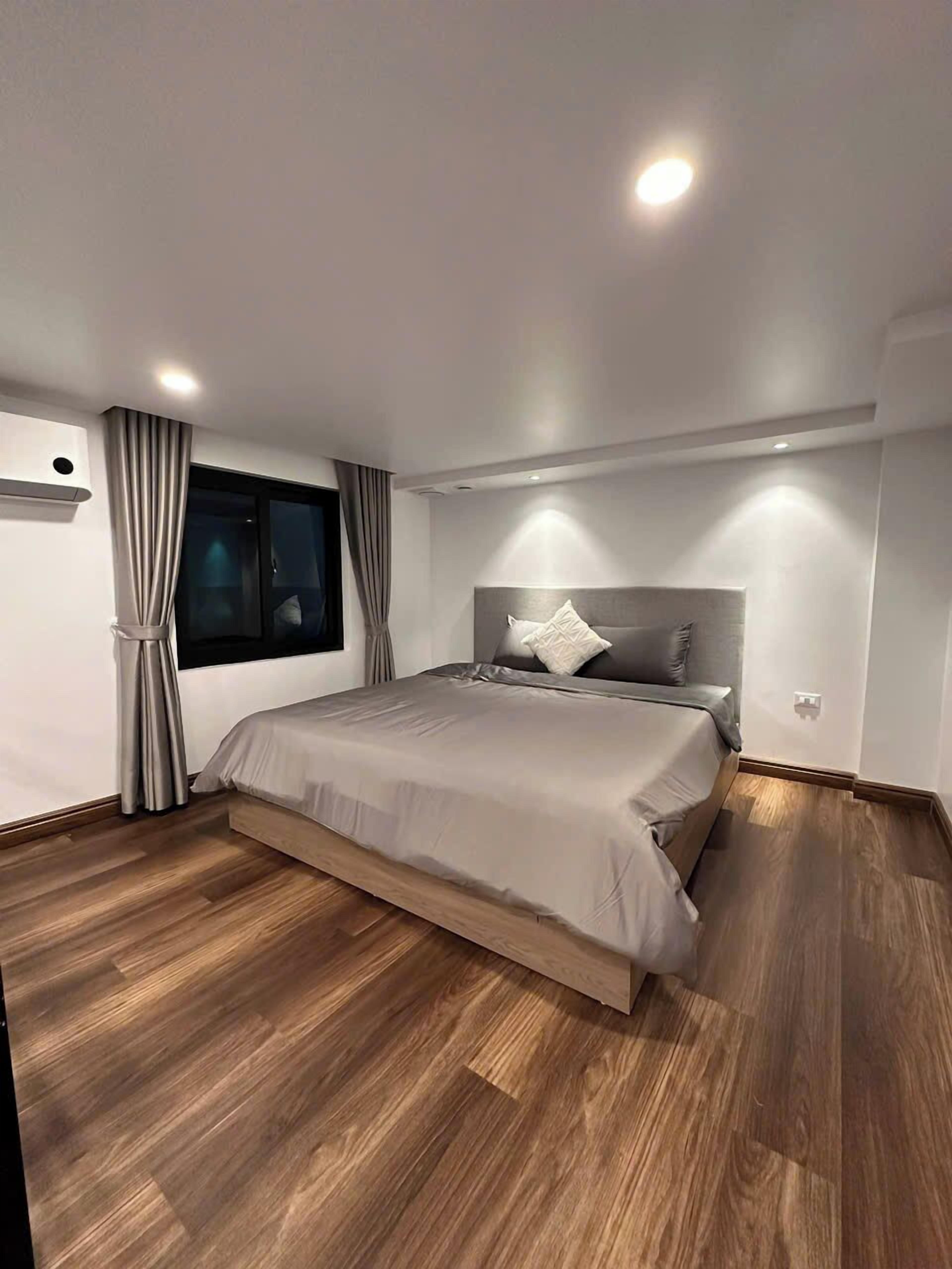 Un dormitorio moderno con una cama grande, suelo de madera y una ventana con cortinas.