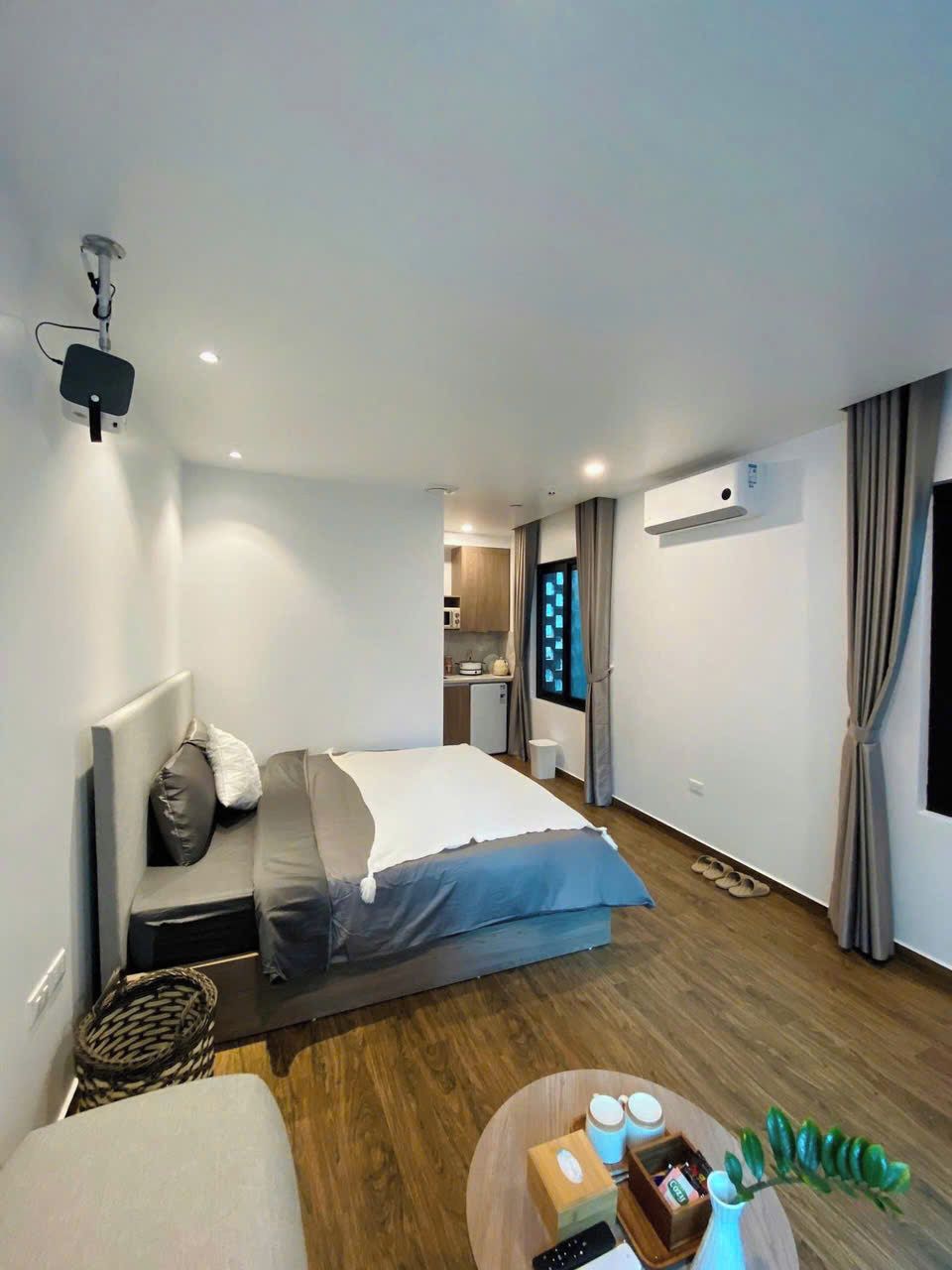 Et moderne hotelværelse med seng, lille tekøkken, loftsvifte og et vindue med gardiner.
