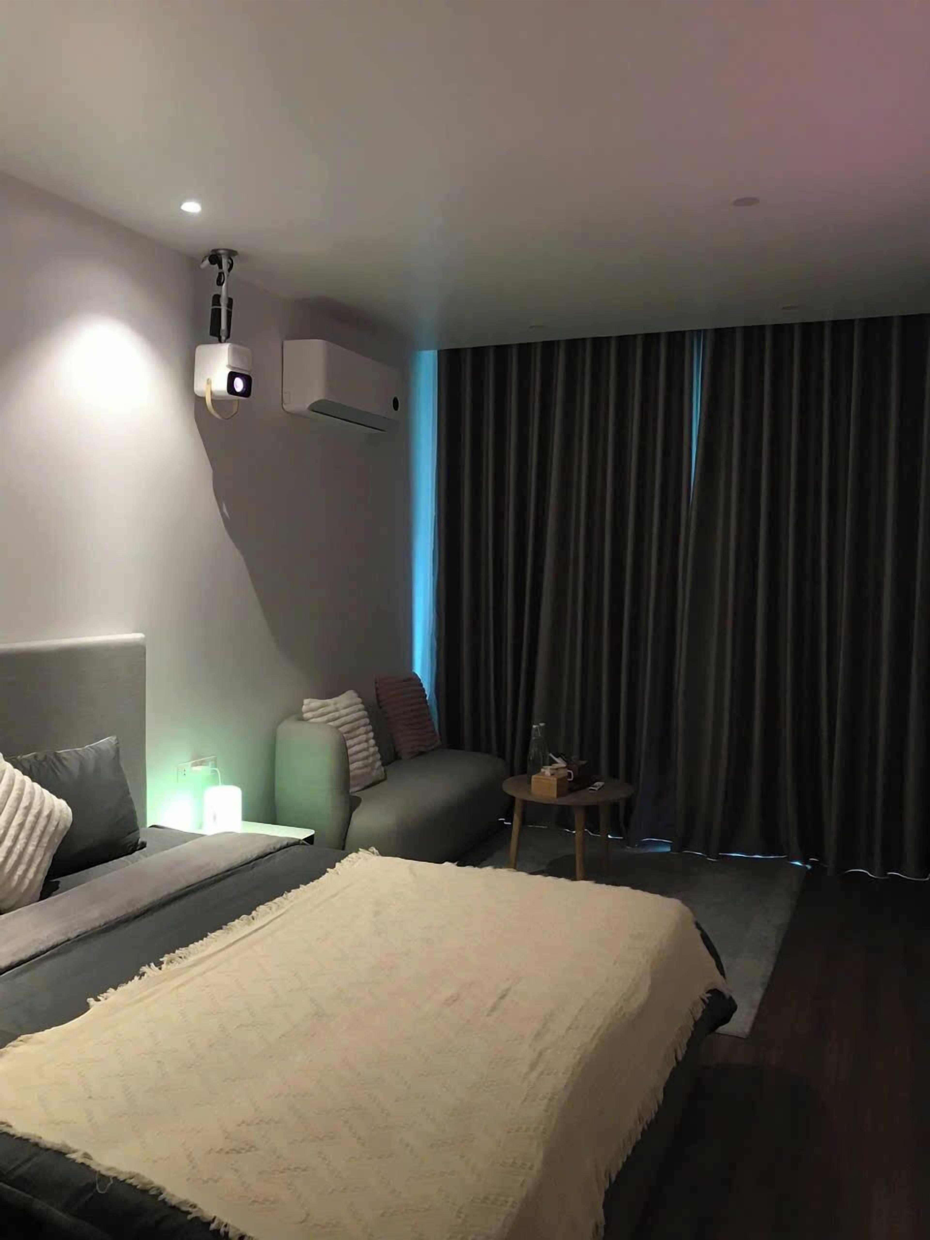 A modern hotel room with a large bed, a sofa, a small table, and a wall-mounted air conditioner.