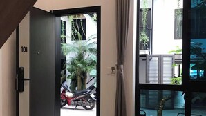 Un intérieur moderne avec un plancher en bois, une table ronde agrémentée d’un vase et d’une boîte, et une grande fenêtre donnant sur une moto garée à l’extérieur.