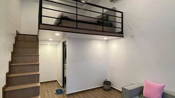 Un espacio habitable moderno con escalera de madera, zona superior con barandilla negra, sofá gris y una pequeña mesa redonda con objetos decorativos.