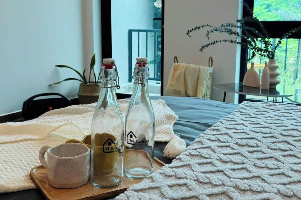 A neatly arranged bed with a textured white blanket, two glass bottles with labels, a white mug, and a wooden tray.