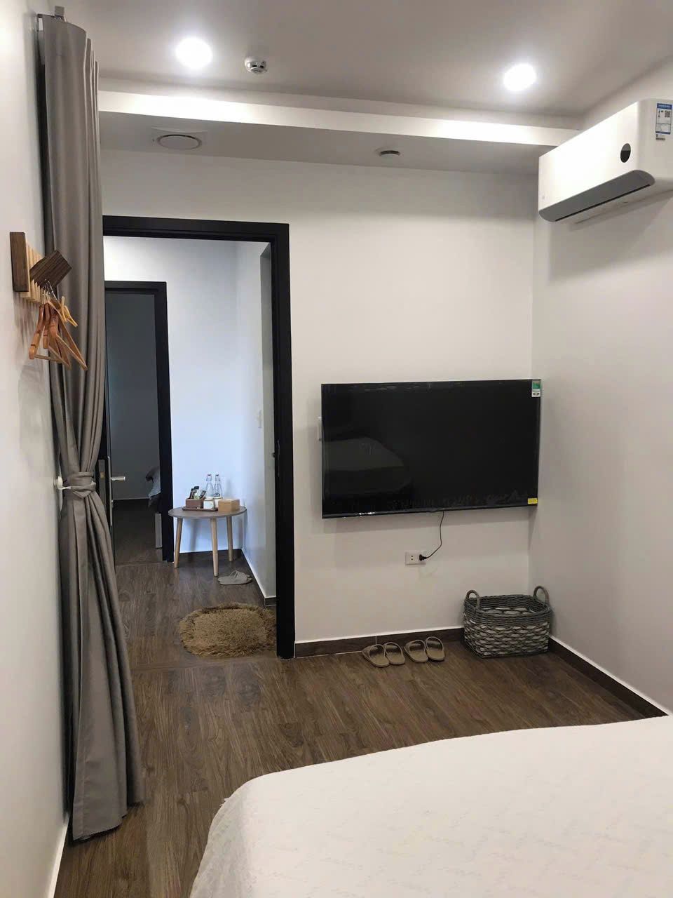 A hotel room with a large bed, a flat-screen TV mounted on the wall, a wooden floor, and a grey curtain.