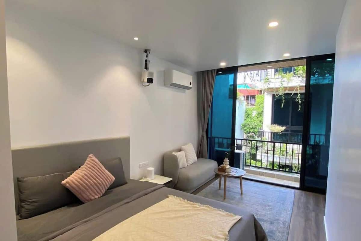 A modern bedroom with a large bed, a sofa, and a balcony with a view.
