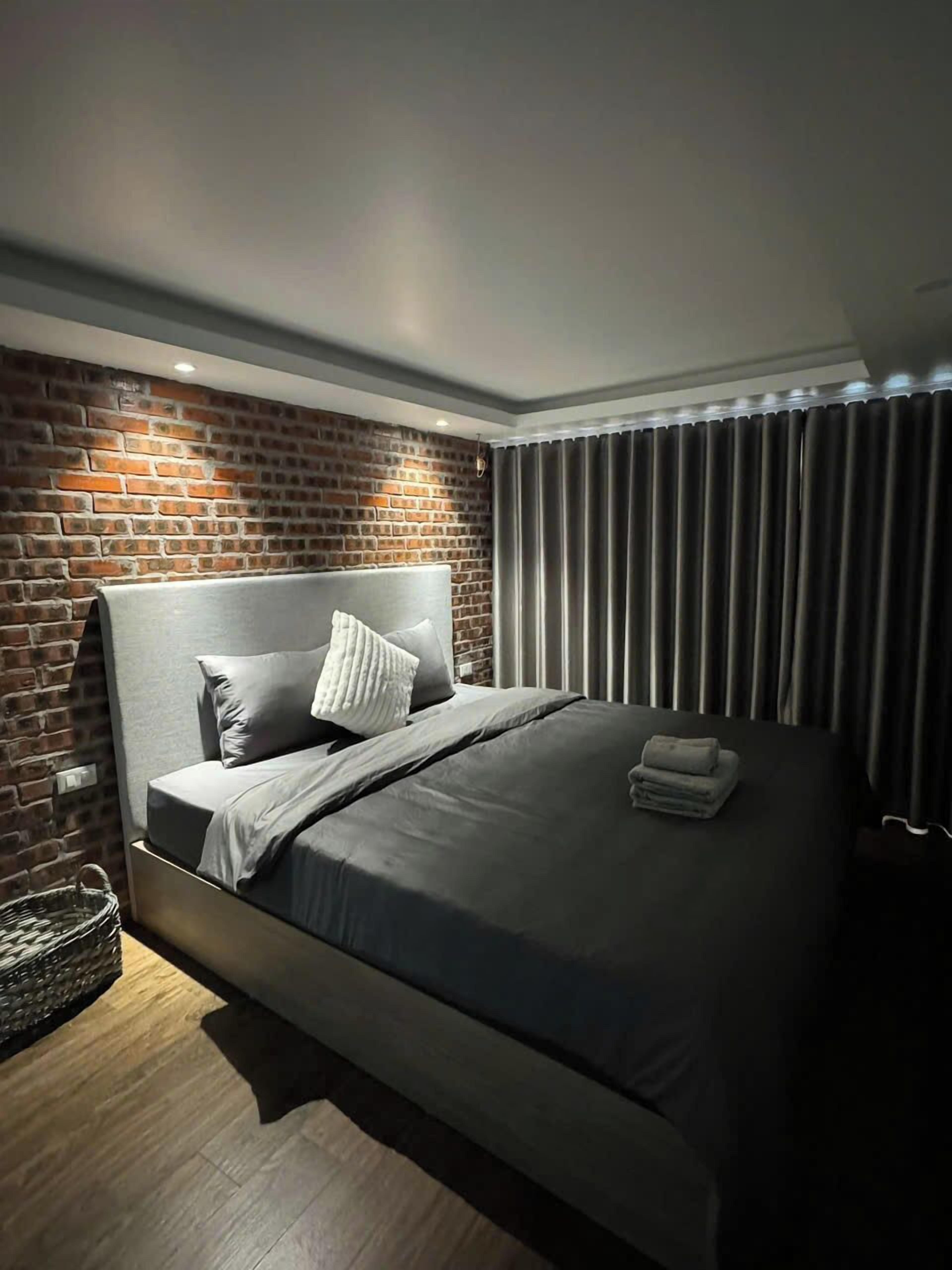 Ein modernes Schlafzimmer mit Backsteinwand, grauem Kopfteil und einem ordentlich bezogenen Bett mit grauem Bettzeug.