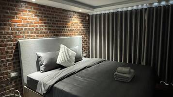 Ein modernes Schlafzimmer mit Backsteinwand, grauem Kopfteil und einem ordentlich bezogenen Bett mit grauem Bettzeug.
