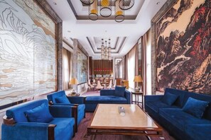 Um hall amplo com sofás azuis, uma mesa de centro de madeira e grandes murais nas paredes.