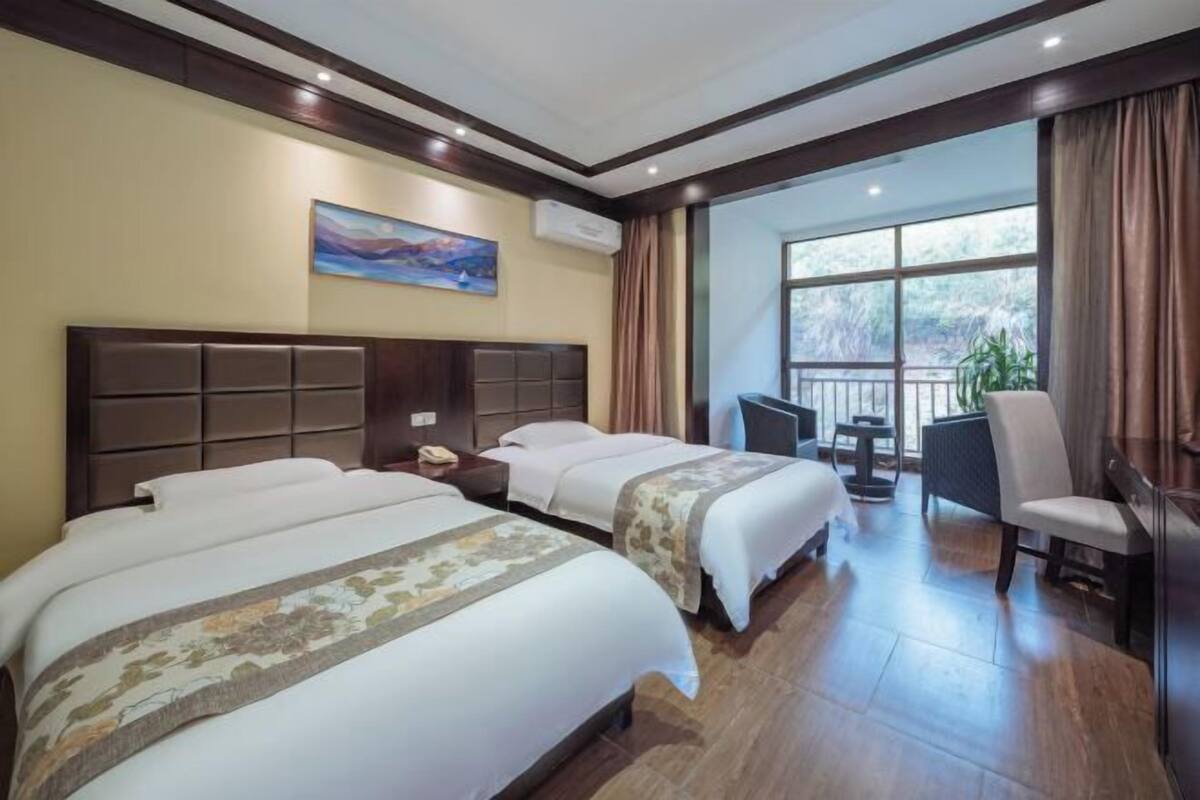 A hotel room with two beds, a desk, a chair, and a large window.