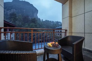 A balcony with wicker furniture, a small table with fruit, and a view of a mountain.