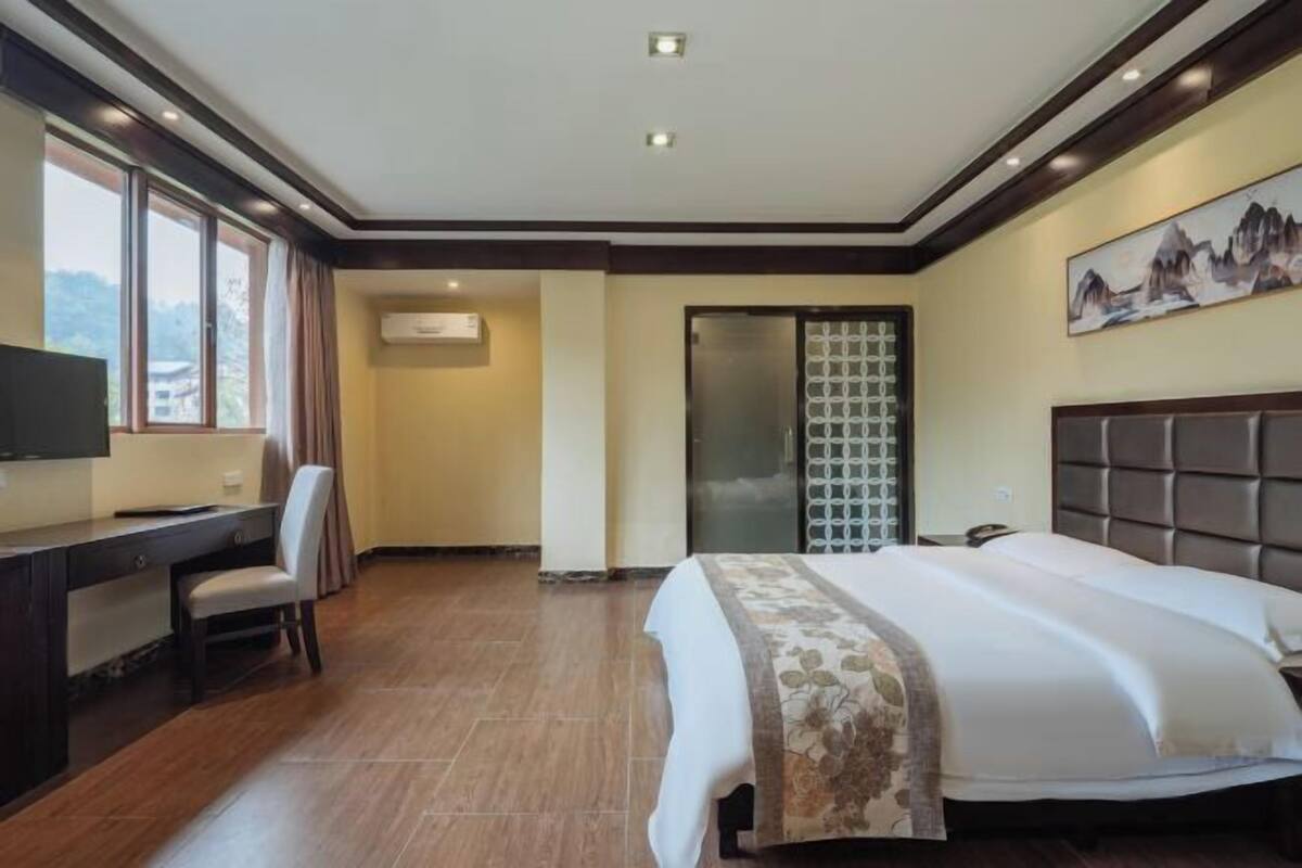 A hotel room with a bed, desk, chair, and a painting on the wall.