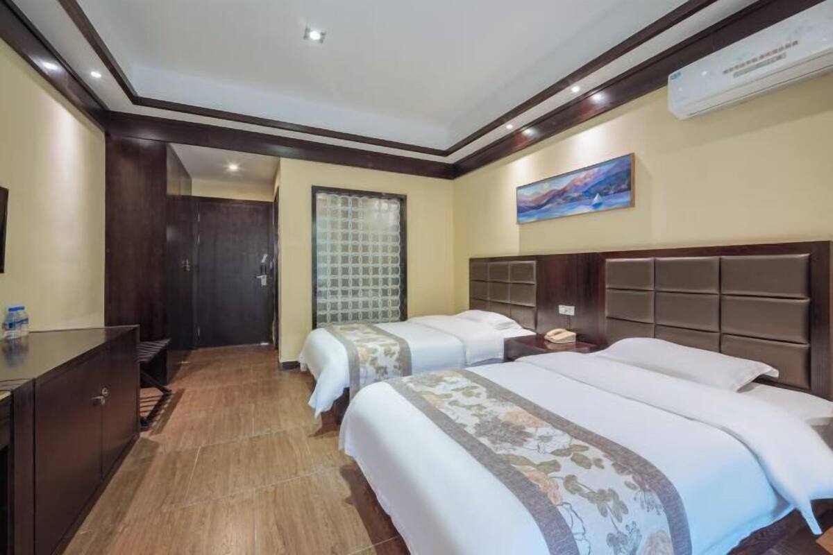 A hotel room with two beds, a desk, a cabinet, a window with a view, and a painting on the wall.