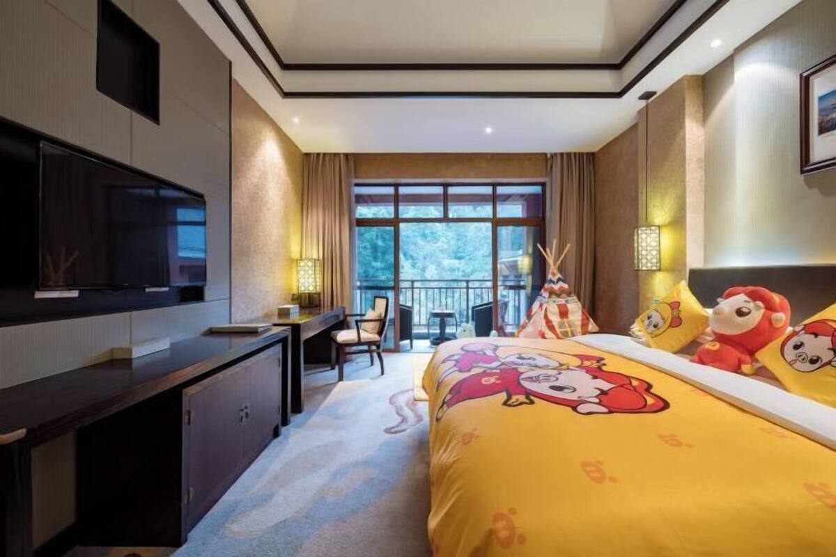 A hotel room with a bed, desk, TV, and large windows.