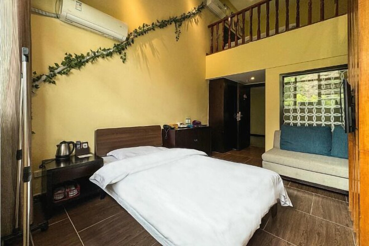 A hotel room with a bed, a nightstand, a window with blinds, a sofa, and a staircase.