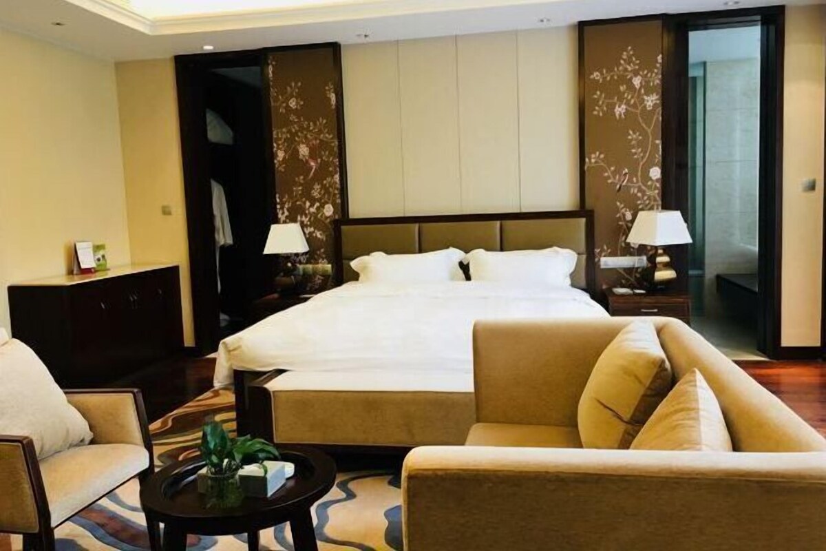 A hotel room with a large bed, two bedside tables with lamps, a sofa, and a small coffee table.