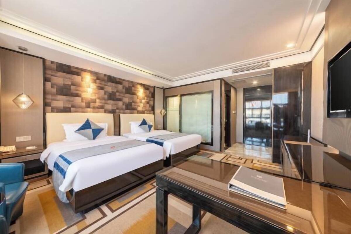 Une chambre d’hôtel moderne avec deux lits, une table basse en verre et un grand téléviseur.
