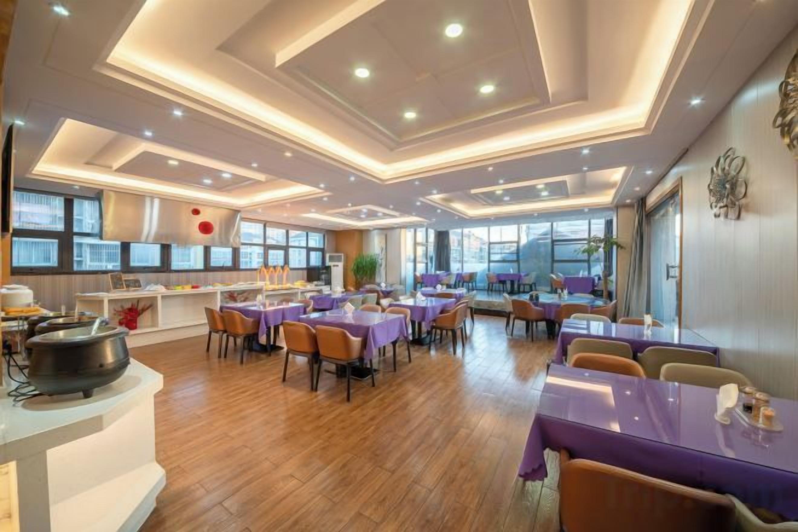 A restaurant with multiple tables and chairs, a kitchen area, and a modern ceiling design.