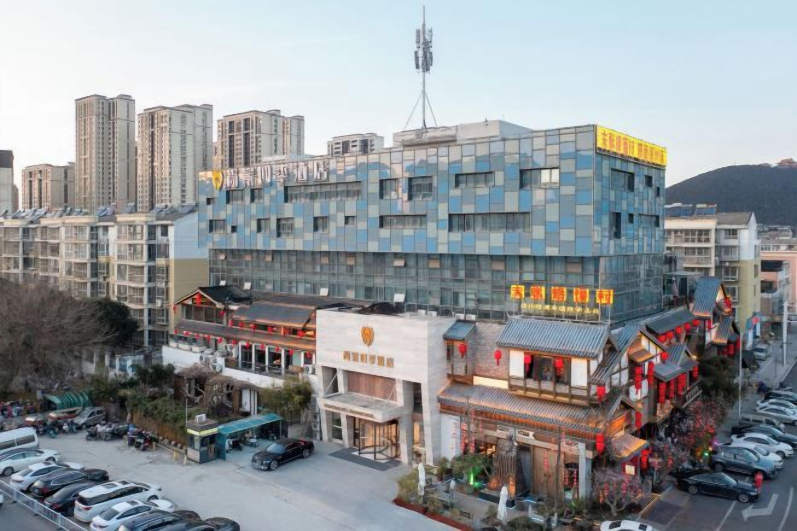 A modern building with a glass facade, surrounded by traditional architecture and a parking lot.