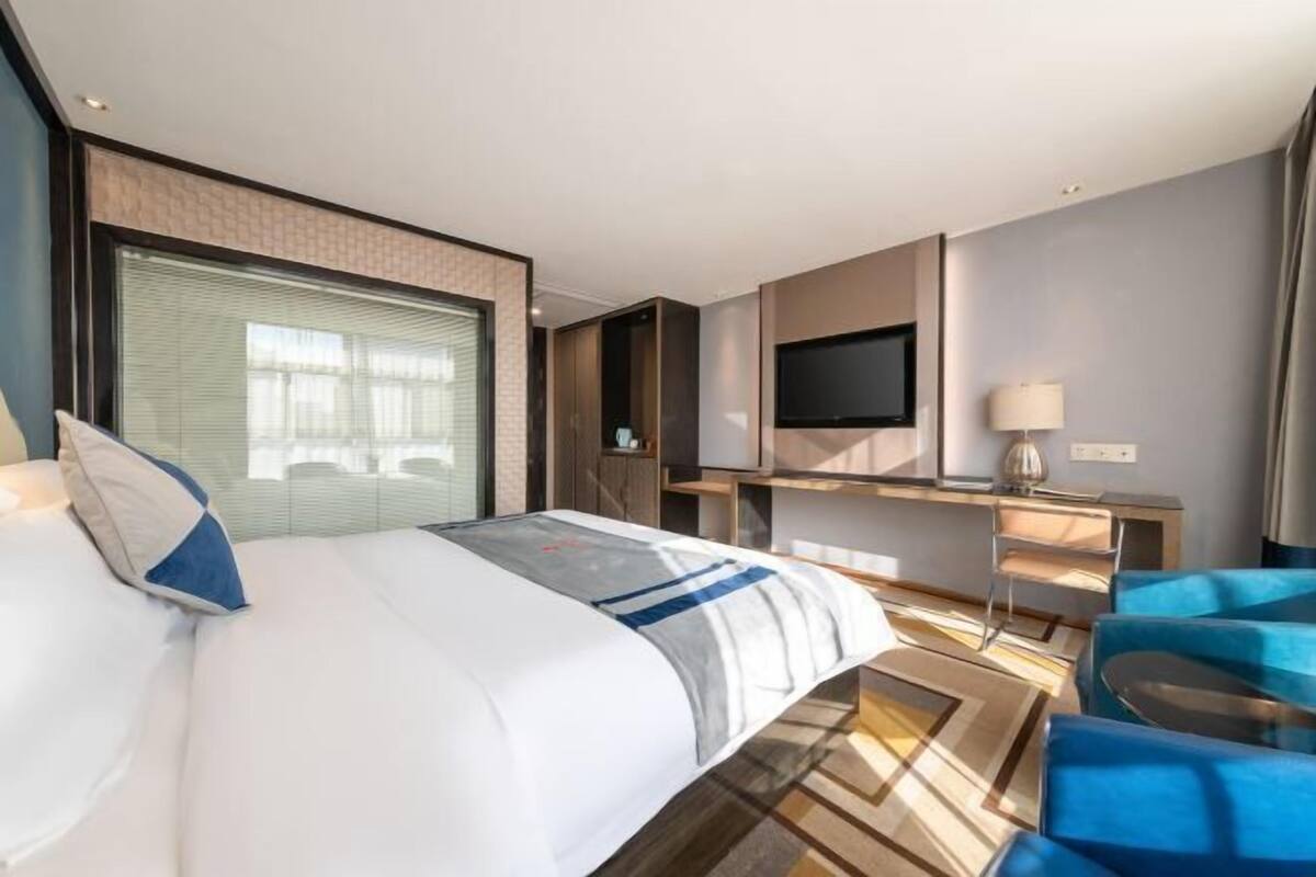 Une chambre d’hôtel moderne dotée d’un grand lit, d’un bureau avec un téléviseur à écran plat et d’un coin salon avec des chaises bleues.