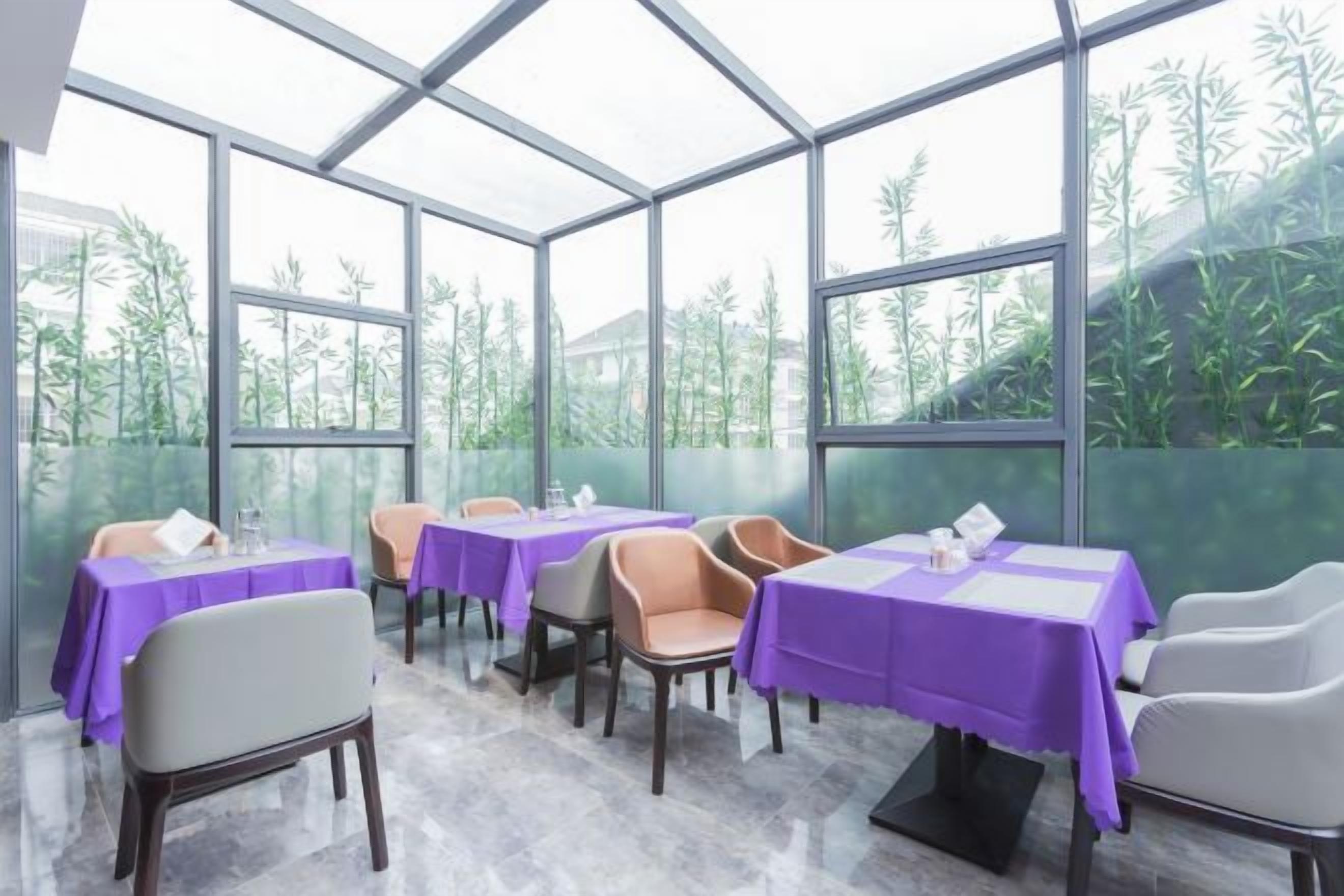 A restaurant with tables covered in purple tablecloths, chairs, and a glass enclosure with a view of greenery.