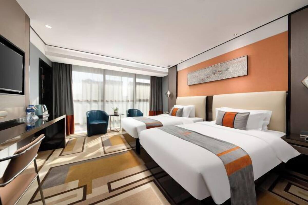 Une chambre d’hôtel avec un grand lit, deux petits lits, un bureau, une chaise et un téléviseur.