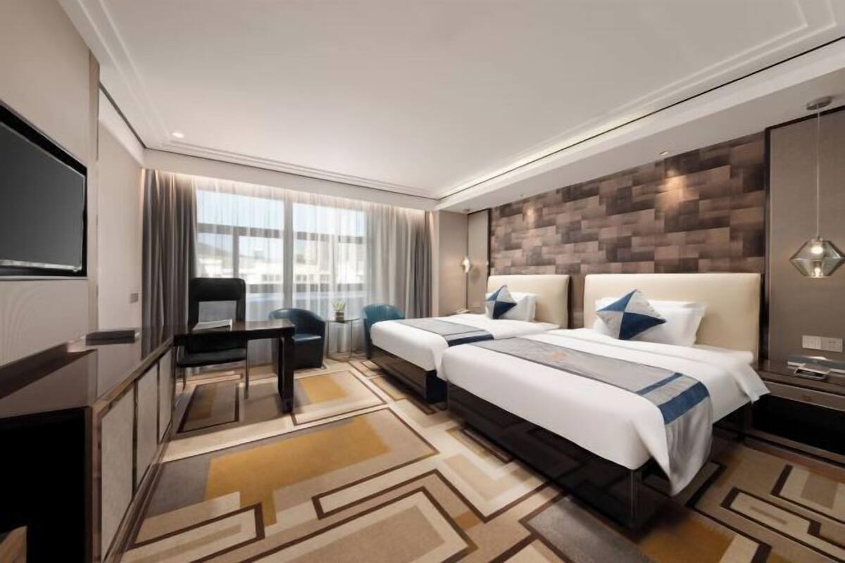 Une chambre d’hôtel avec deux lits, un bureau, une chaise, une télévision et une grande fenêtre.