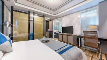 Ein modernes Hotelzimmer mit einem großen Bett, einem Schreibtisch, einem Fernseher und einem durch eine Glastür einsehbaren Badezimmer.