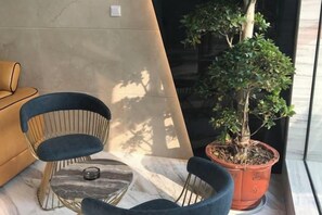 A potted tree, a round marble table, and two chairs with a sofa in the background.