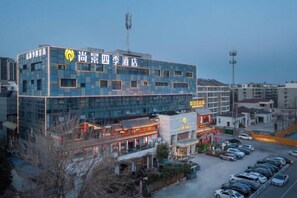A multi-story hotel with a modern glass facade, a parking lot, and a visible restaurant on the ground floor.
